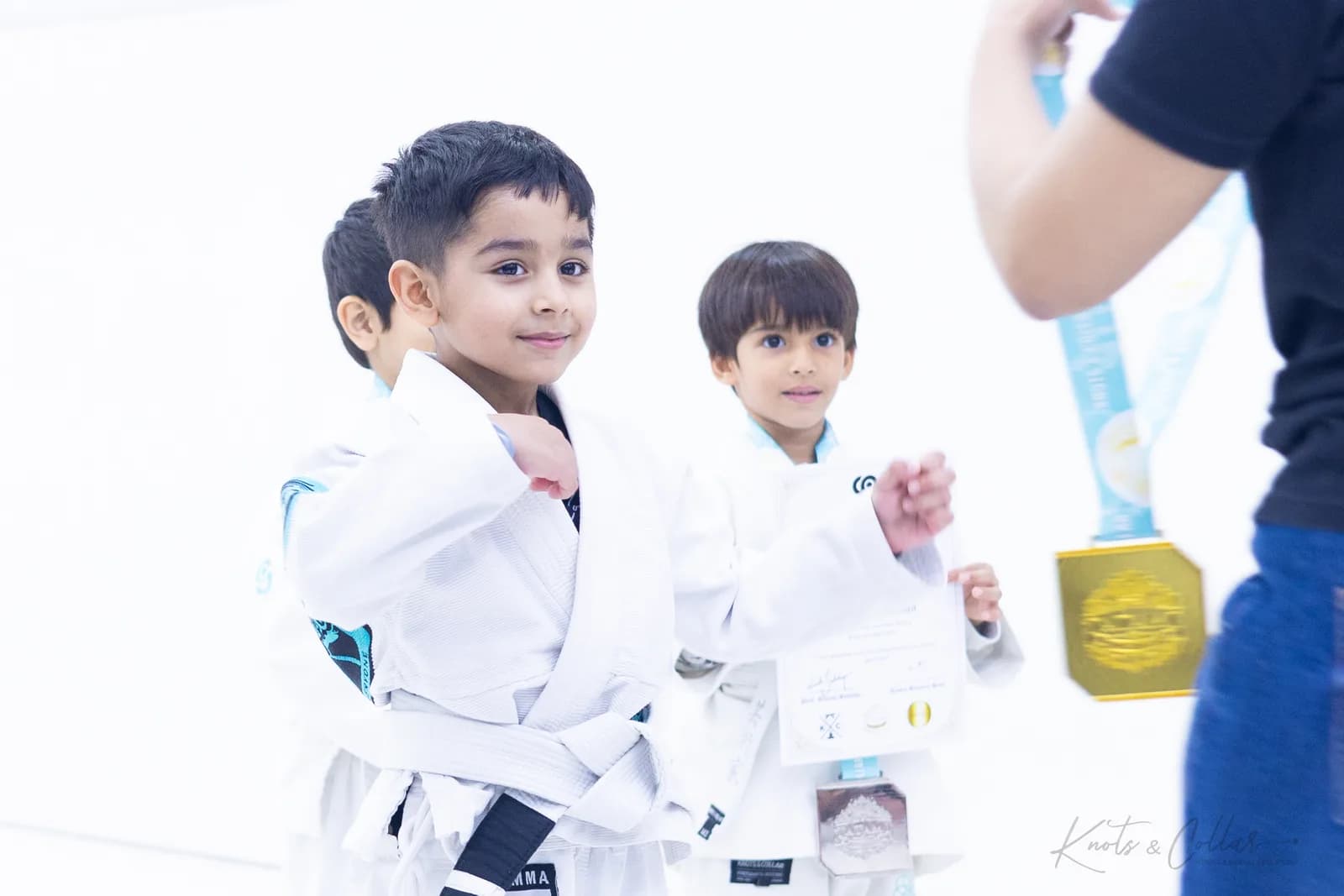 Two young Knots & Collar students in white gis with their Brazilian Jiu-Jitsu grading certificate and medal at the kids BJJ class in Defence Colony, New Delhi