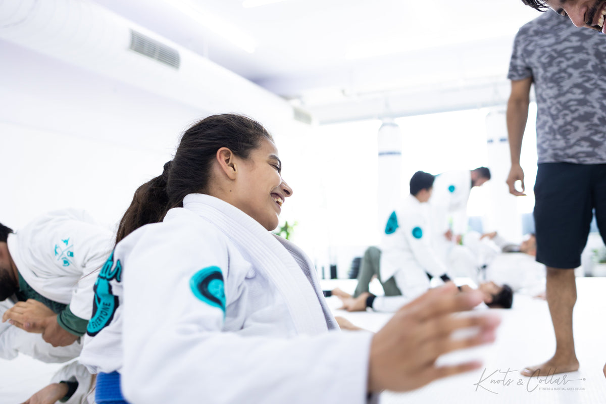 Woman training BJJ for fitness, smiling during a live rolling session