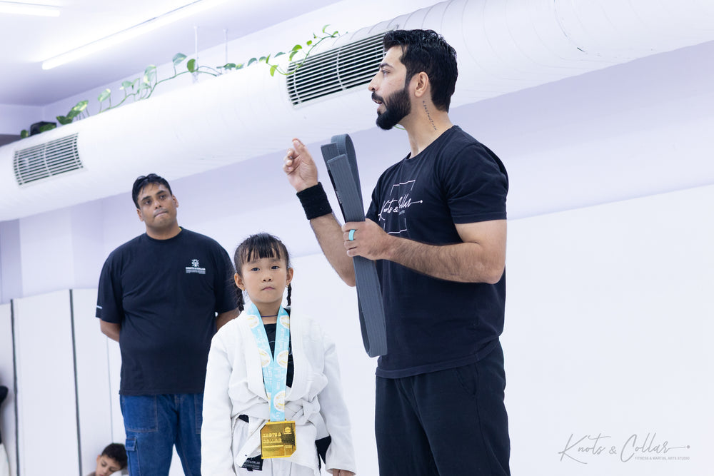 Kids BJJ belt promotion ceremony — young student receiving a medal and certificate